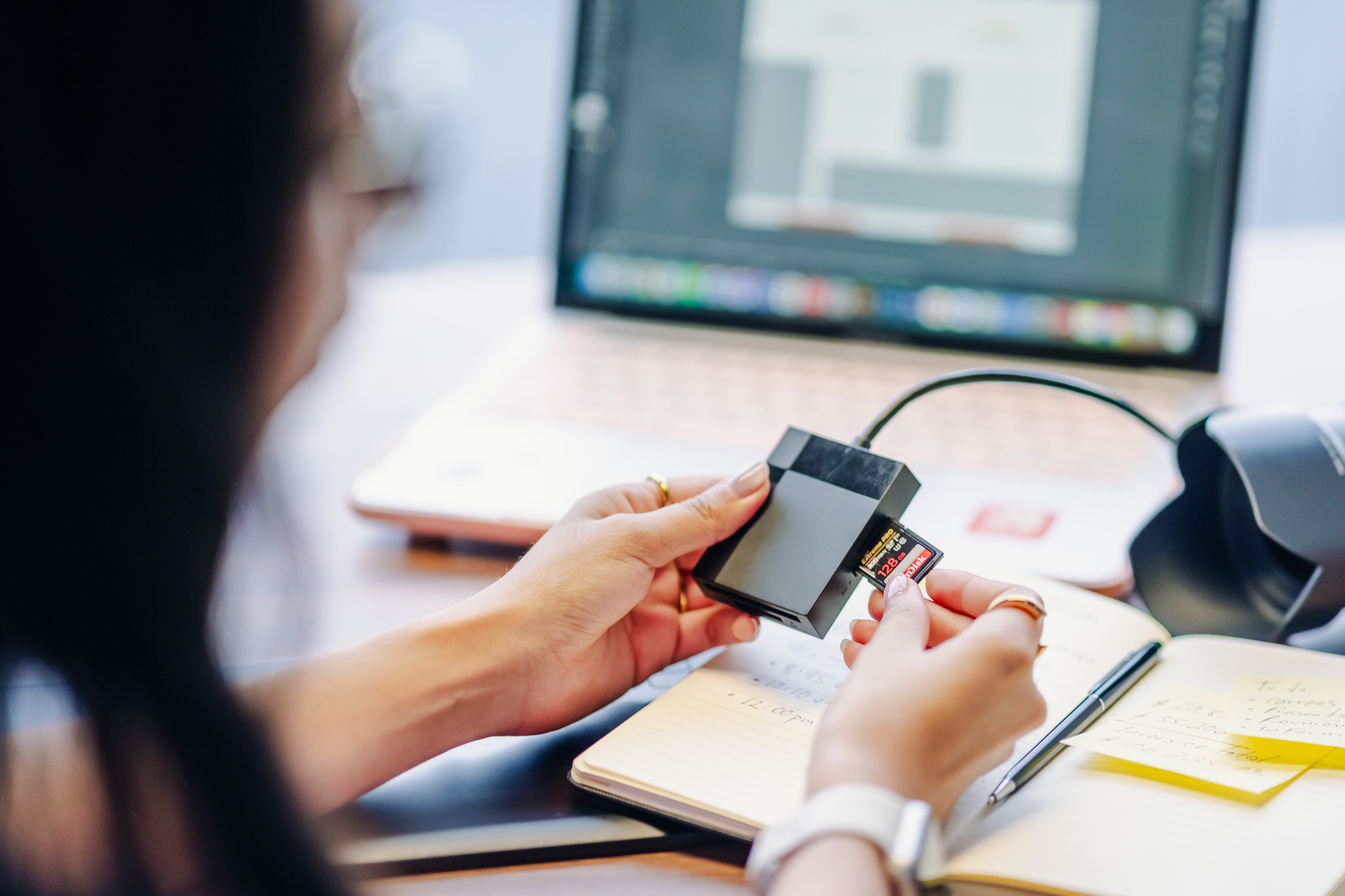 Une personne insère une carte SD dans un lecteur à côté d’un ordinateur portable sur un bureau
