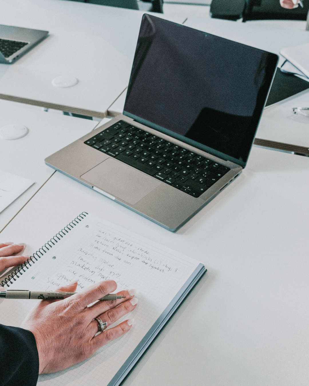 Un employé prend des notes sur un carnet devant son ordinateur portable